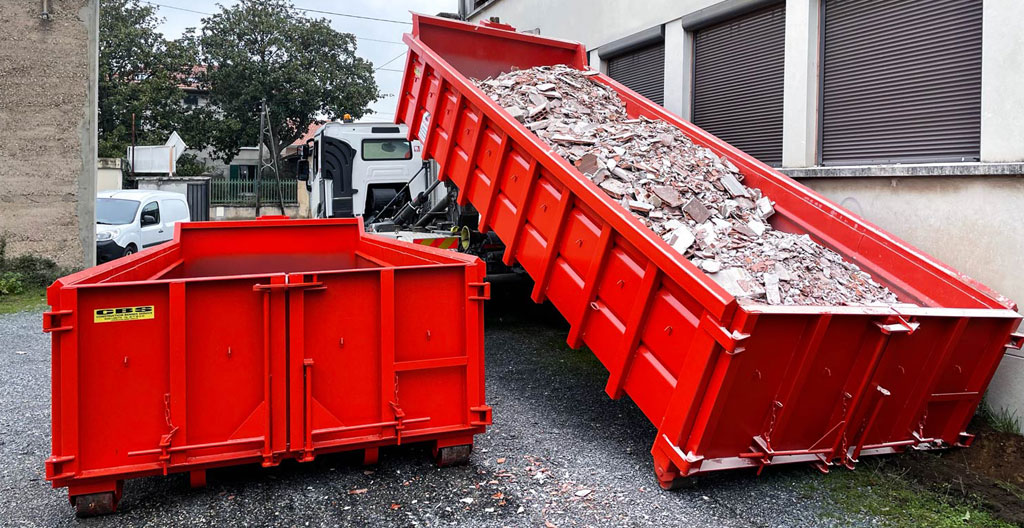 Goulotte d'évacuation de gravats orange installée le long de la façade d'un immeuble haussmannien parisien en pierre de taille, débouchant dans une benne de chantier au niveau de la rue